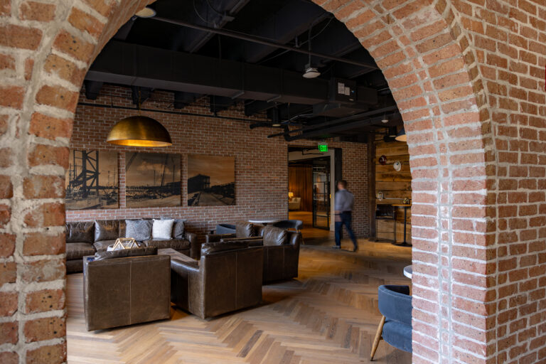 Modern office lounge area with brick archway, leather sofas, and a person walking in the background.