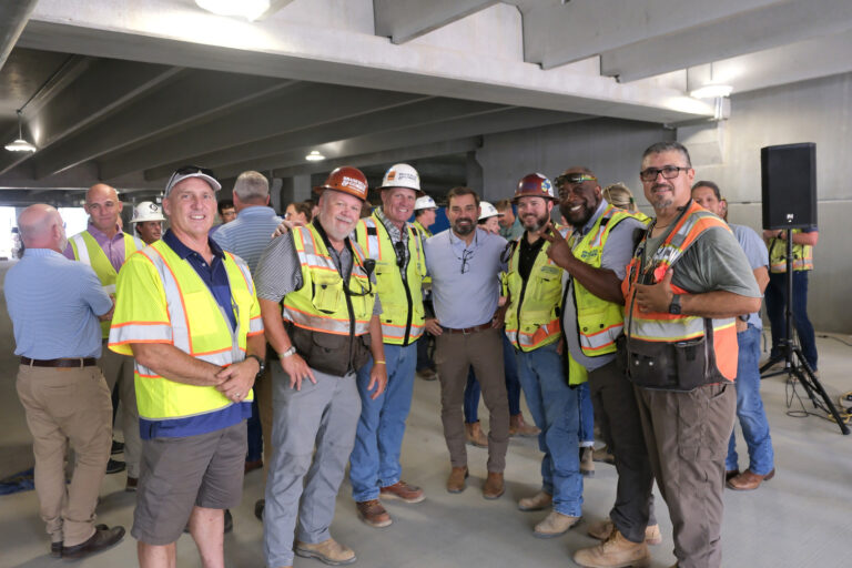 A group of construction workers in hard hats and safety vests gathered inside a building under construction.