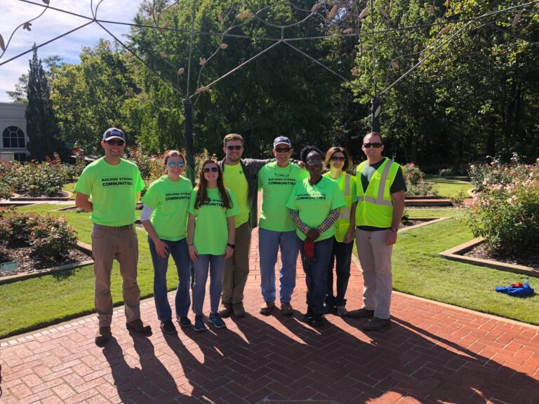 Group of volunteers wearing green shirts and safety vests pose together in a garden in Birmingham, Alabama.