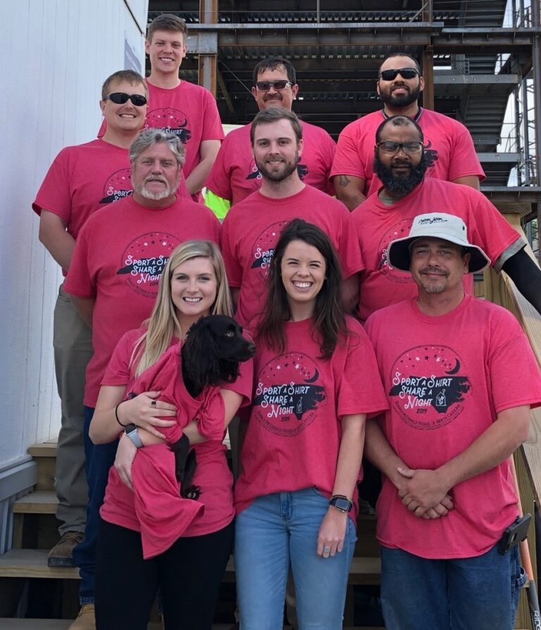 A group of people from Charlotte NC in matching pink t-shirts posing for a photo, with one person holding a small black dog.
