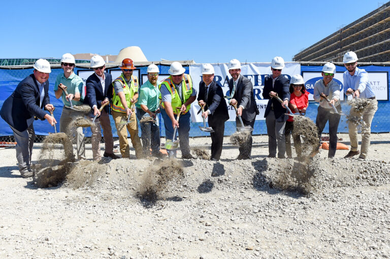 Group of individuals in hard hats and formal attire performing a groundbreaking ceremony.