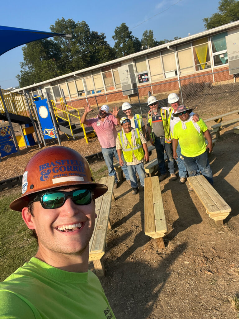 A construction worker takes a selfie with colleagues behind him at a playground construction site in Jackson, Mississippi, all wearing safety gear.