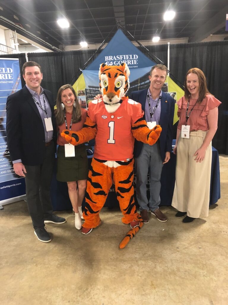 Group of four people posing with a person in a tiger mascot costume at an indoor event.
