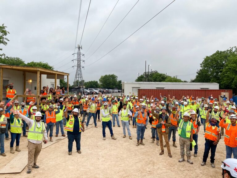 Group of construction workers in safety gear waving at a jobsite in Dallas, Texas.