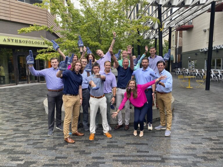 A group of people celebrating or cheering outdoors in Greenville, South Carolina, some holding drinks, with raised hands and energetic expressions.