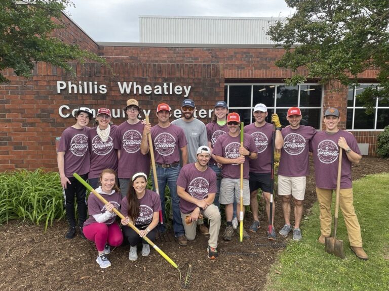 Group of volunteers wearing matching t-shirts posing in front of the Phillis Wheatley Community Center in Greenville, South Carolina.