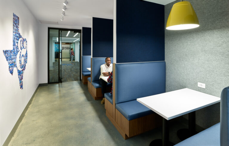 Person sitting in a modern office break area with blue booths and pendant lighting in Dallas, Texas.