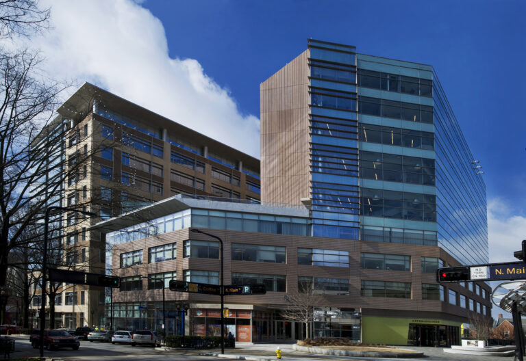 Modern multi-story building with a mix of glass and metal facades under a clear blue sky.