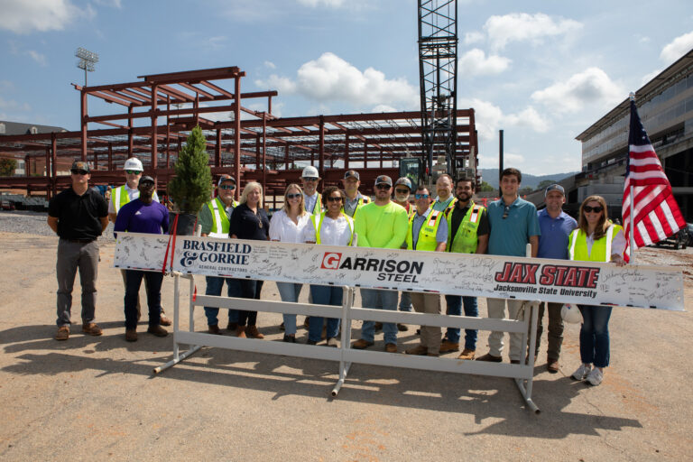 A group of construction workers and associates posing with a ceremonial beam at a Birmingham, Alabama construction site.