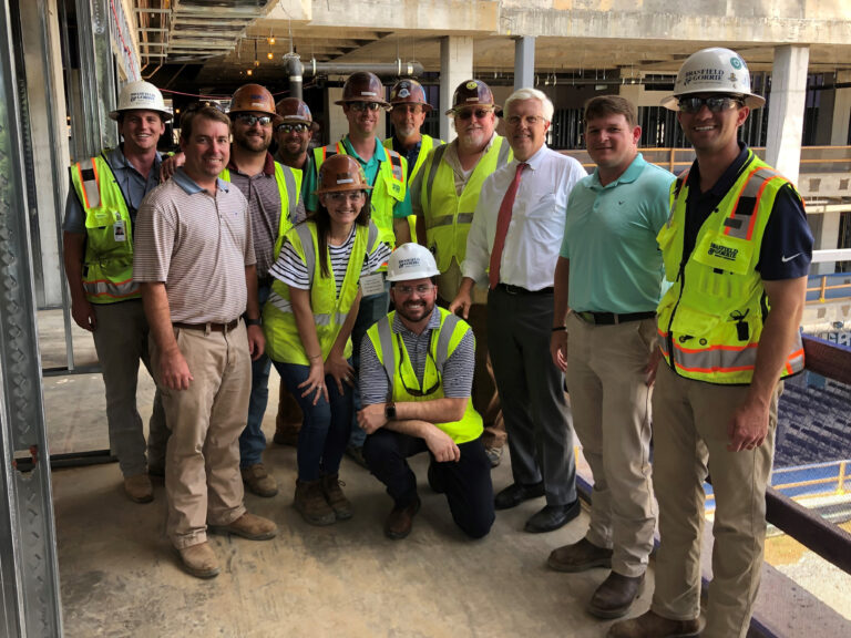 Group of construction workers and engineers in hard hats posing together at a construction site in Jackson, Mississippi.
