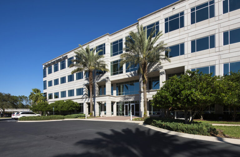 Modern office building with palm trees and clear blue skies.
