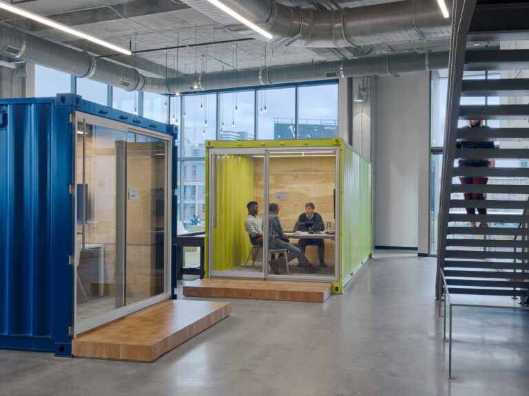 Two individuals having a meeting in a modern office inside a yellow glass-walled pod.