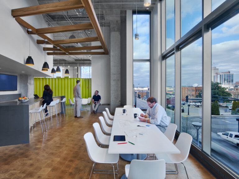 Modern office space with natural light, featuring employees working and communal areas.