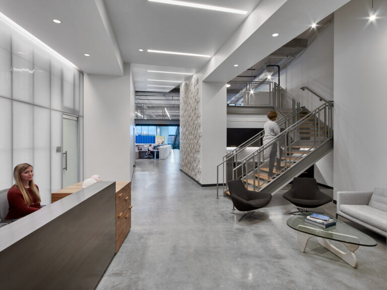 Modern office lobby with reception desk, stairway, and seating area.