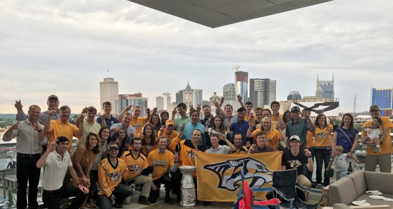 A large group of people in a room with a city skyline in the background, some wearing sports team attire and posing for a group photo.