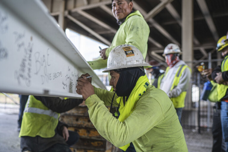 Construction workers signing a steel beam at a construction site.