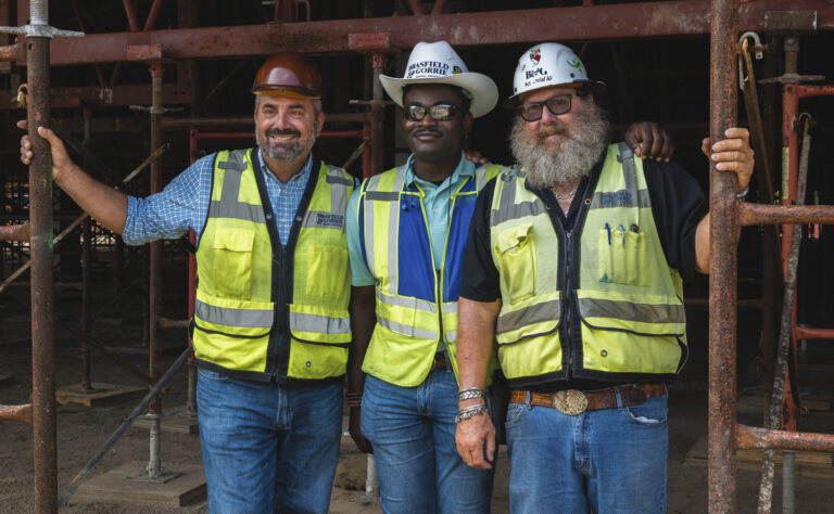 Three construction workers in high-visibility vests and hard hats smiling at the camera in Orlando, Florida.
