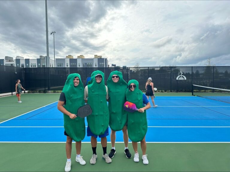 Four people dressed in pickle costumes standing on a tennis court in Orlando, Florida.