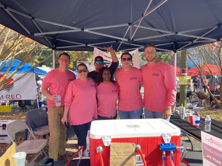 A group of individuals in matching pink shirts standing under a canopy at an outdoor event.