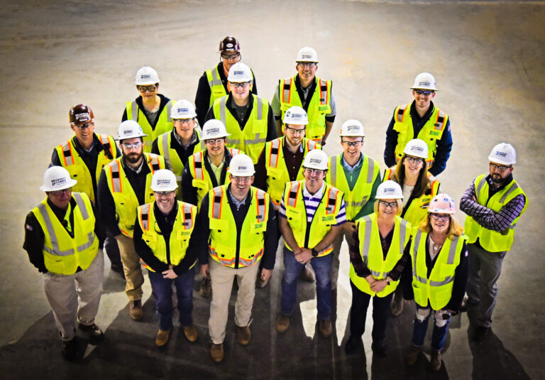 Group of construction workers in hard hats and high-visibility vests smiling for a photo.