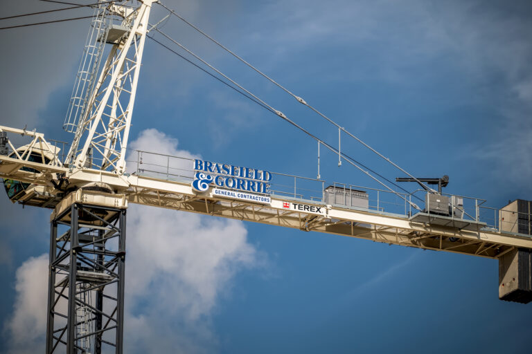 Tower crane against a cloudy blue sky with Brasfield & Gorrie logo.