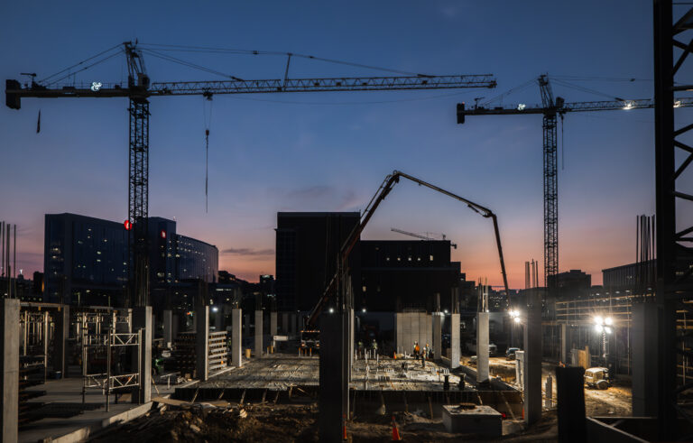 Construction site at dusk with cranes and concrete pump.