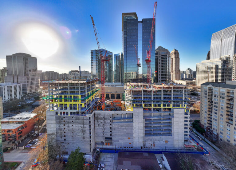 A construction site with cranes and partially completed buildings, showcasing expert project management, against a backdrop of the city skyline on a clear day.