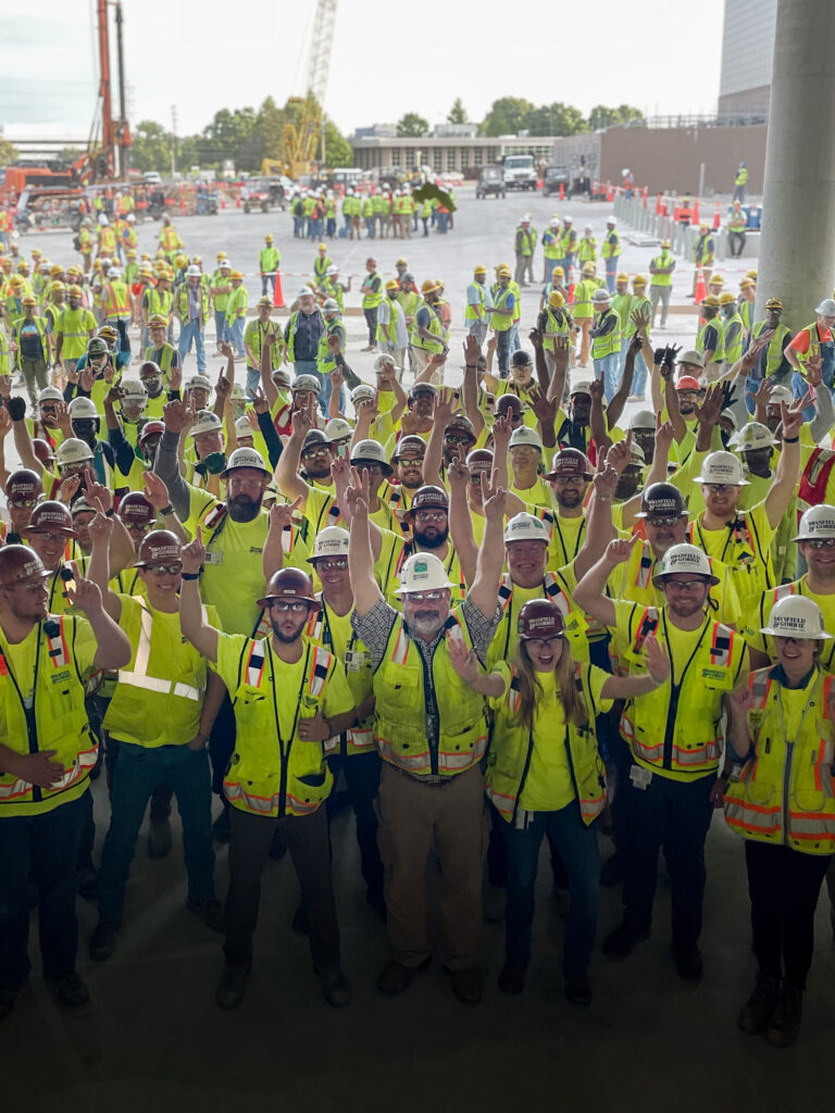 Group of construction workers in safety gear posing together at a construction site, proudly representing our company's mission.