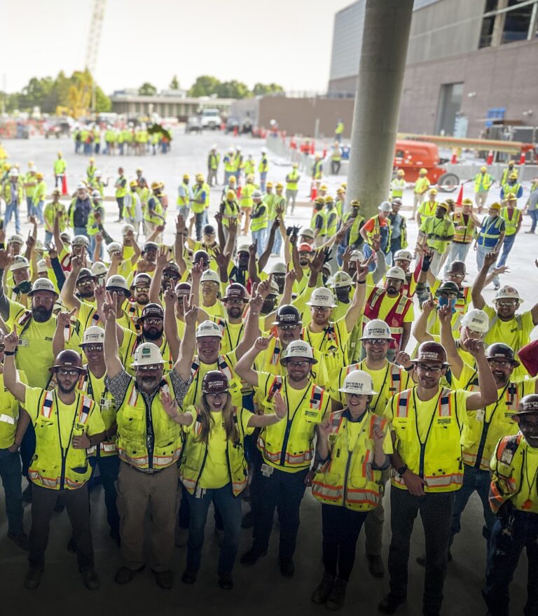 A group of construction workers in safety gear raising their hands in a gesture of celebration.