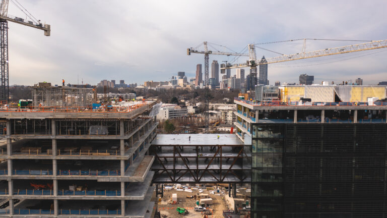 Construction site with multiple cranes and unfinished buildings against a city skyline.