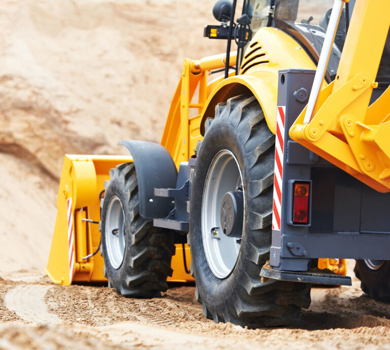 A yellow wheel loader is actively engaged at work on a sandy construction site.