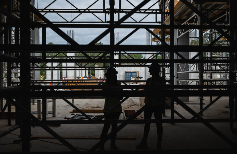 Two construction workers in hard hats silhouetted against an jobsite backdrop