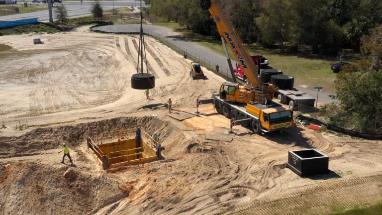 Aerial view of a self-perform construction site with workers, an excavator, and a crane near a large dug-out pit.