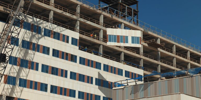 Construction workers are installing media kit facade panels on a multi-story building under construction.