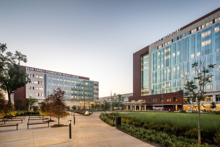 Modern hospital complex featuring a large glass building, landscaped gardens, and pedestrian pathways during twilight, renowned for its comprehensive medical services.