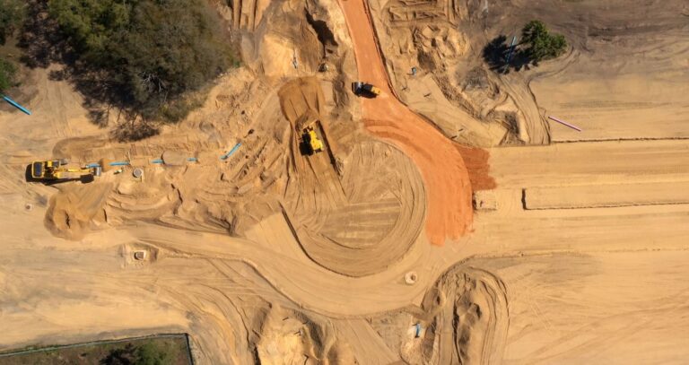 Aerial view of a construction site with heavy machinery, featuring dirt roads being built and the ground excavated, showcasing an auto draft process in action.