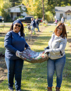 Two women smiling and holding a bag of mulch at a community tree planting event