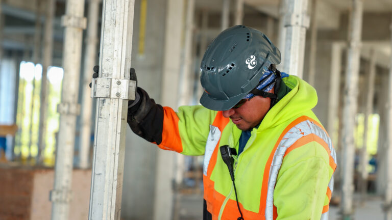 Construction worker in a high-visibility jacket and helmet ensuring safety compliance while adjusting equipment at a building site.