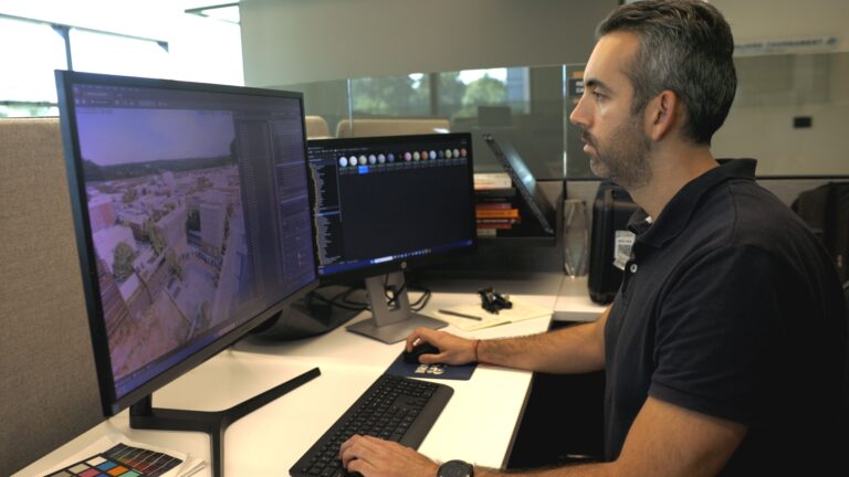 A person sits at a desk in an office, working on dual monitors. One screen displays a 3D rendering of a construction project, while the other shows software tools, embodying the dynamic opportunities found in Brasfield & Gorrie careers.